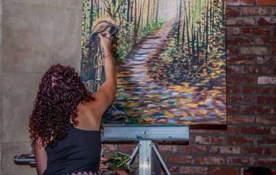 Artist touches up painting of a forest path with fallen leaves.